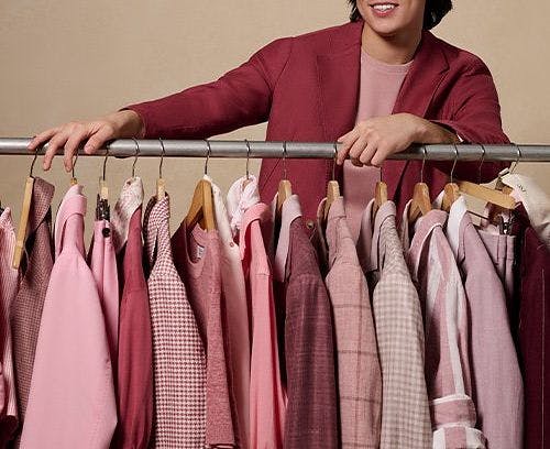 A man standing next to a rack of clothes with pink and red shirts