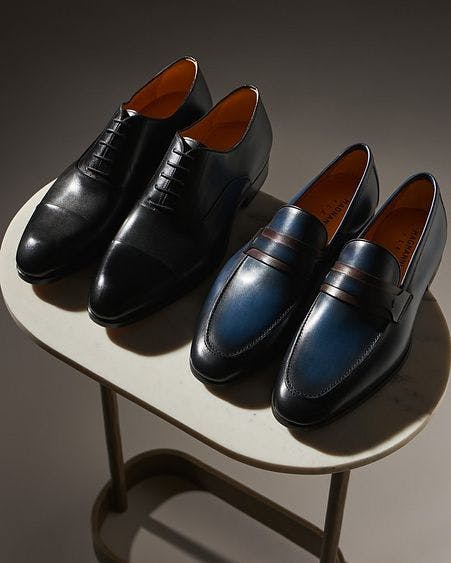 one oxford pair of shoes and one leather loafer pair on table stand