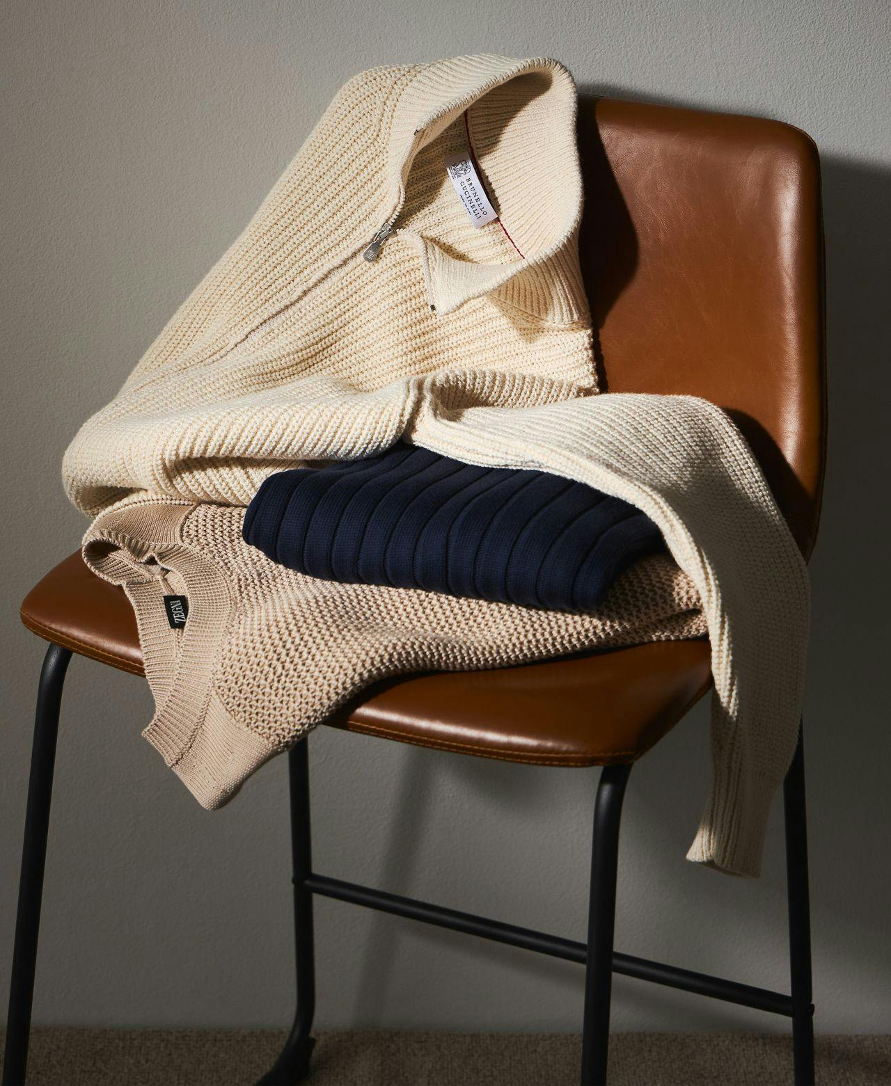 three knit sweaters folded on brown chair