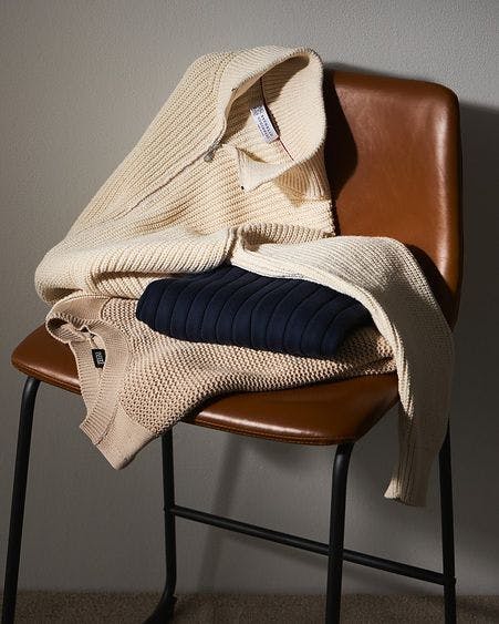 three knit sweaters folded on brown chair