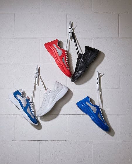 two pairs of sneakers hanging by laces on hook on wall and one sneaker hanging by laces on hook on wall