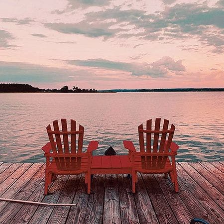 two classic cottage chairs on a wodden dock facing lake in the sunset
