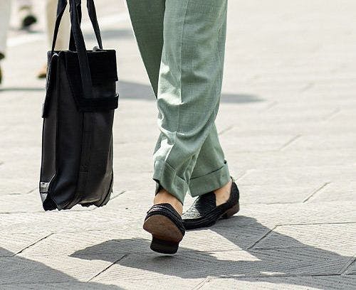 male model holding tote bag, legs walking on street wearing trousers and loafers