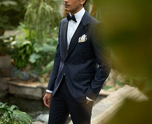 male model outside with hand in pocket wearing suit and bow tie