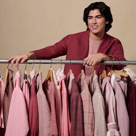 A man standing next to a rack of clothes with pink and red shirts