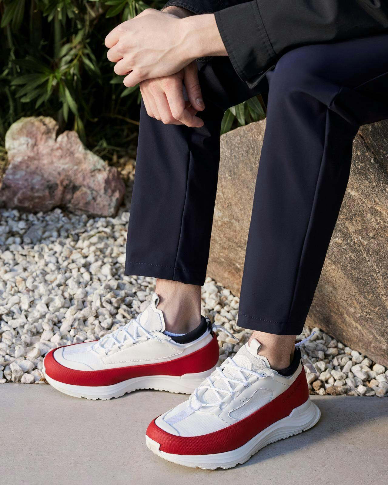 a person sitting on a rock wearing red and white sneakers