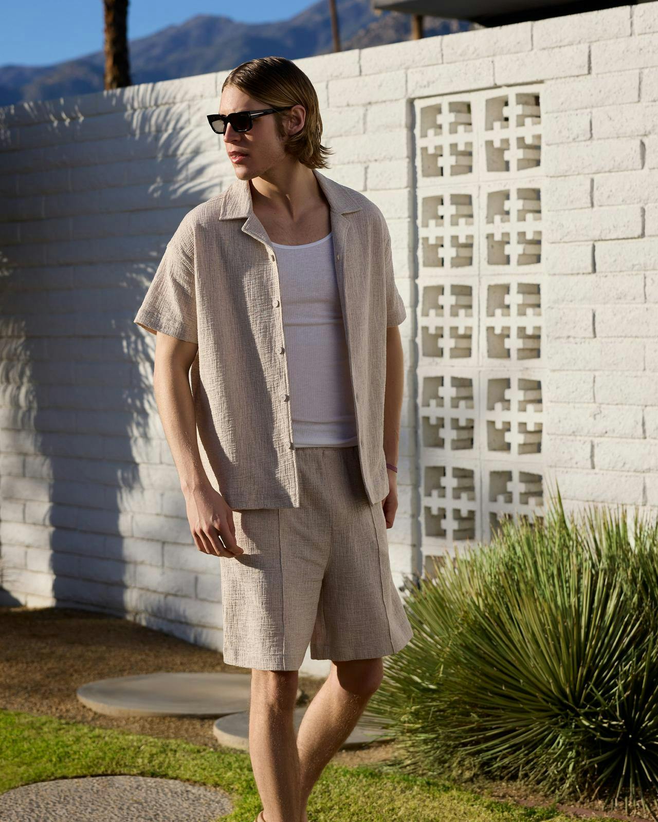 a man in shorts and sunglasses standing in front of a wall