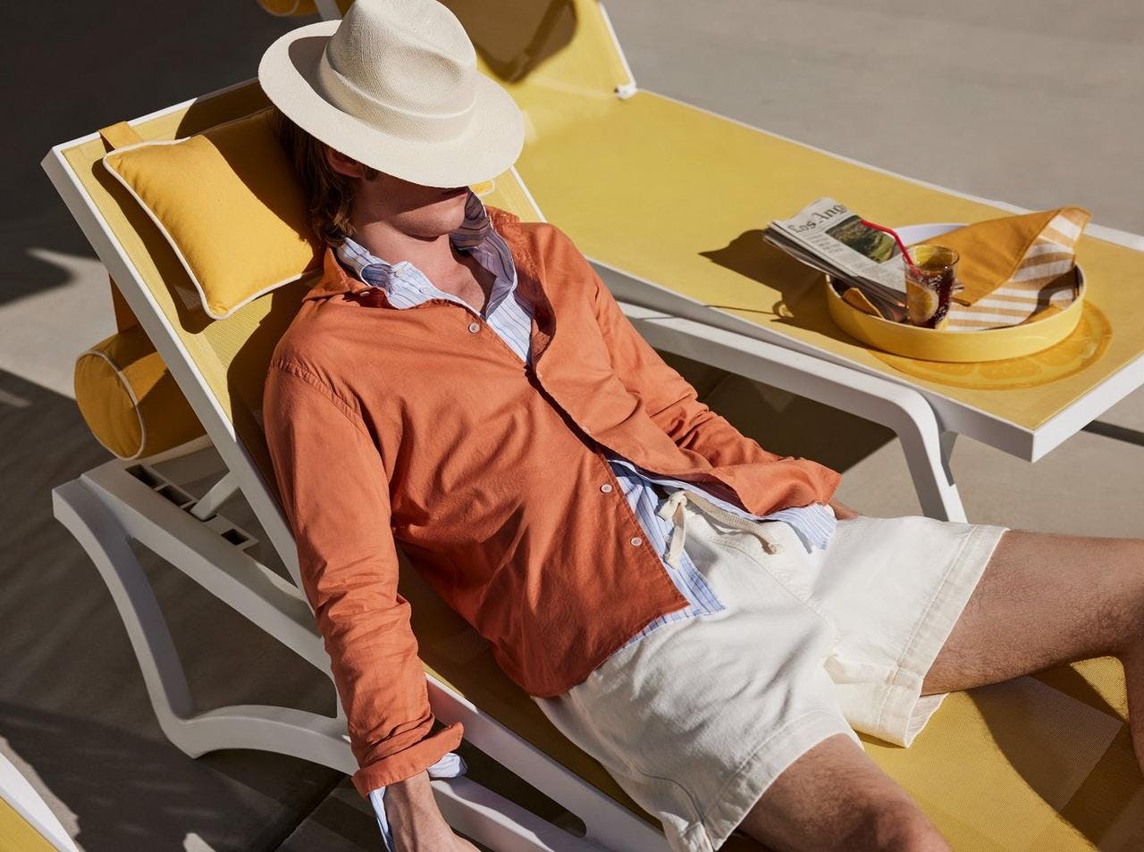 a man in a white hat sitting on a yellow chaise lounge