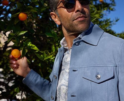A man wearing sunglasses picking an orange