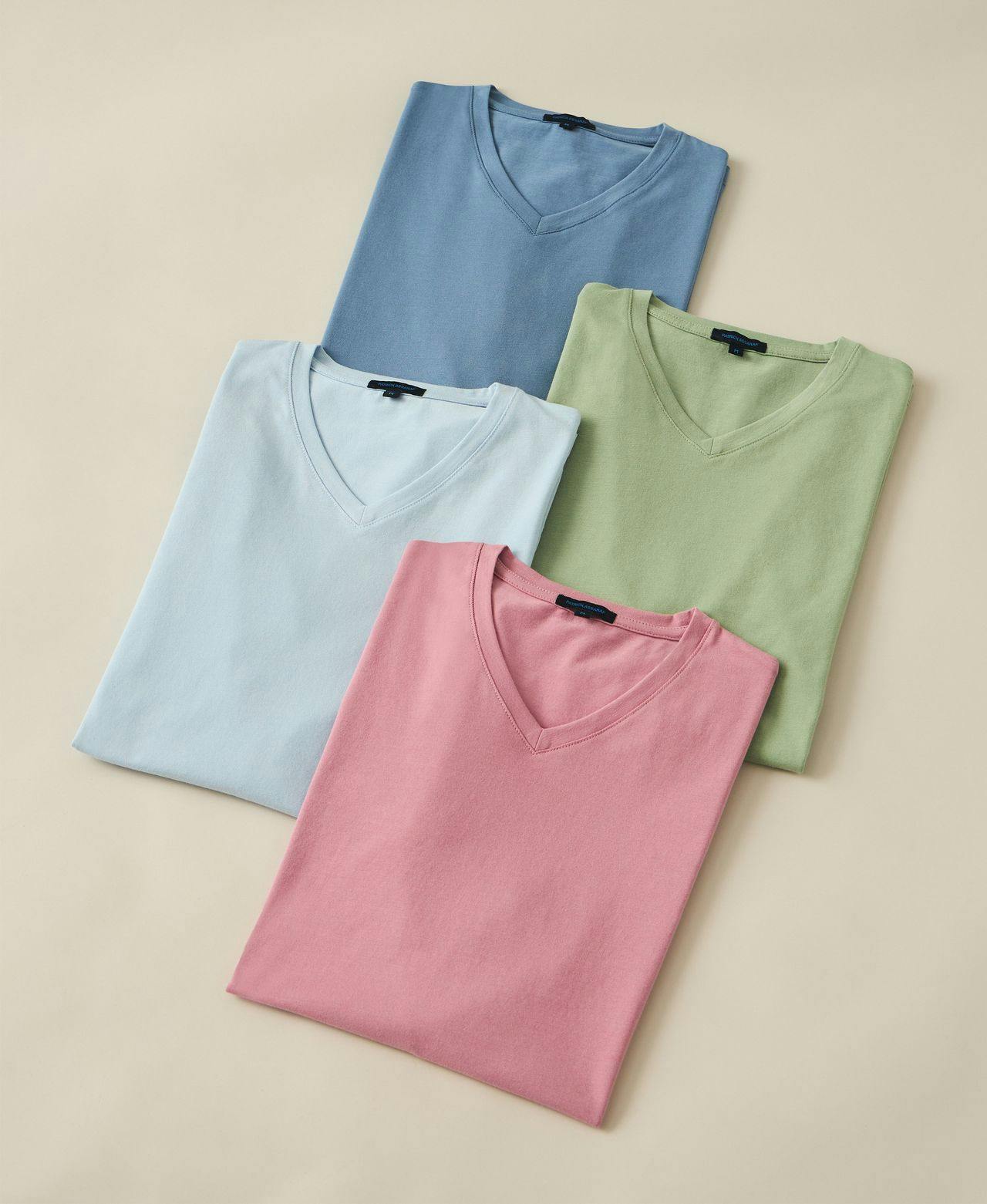 four t-shirts folded on beige backdrop