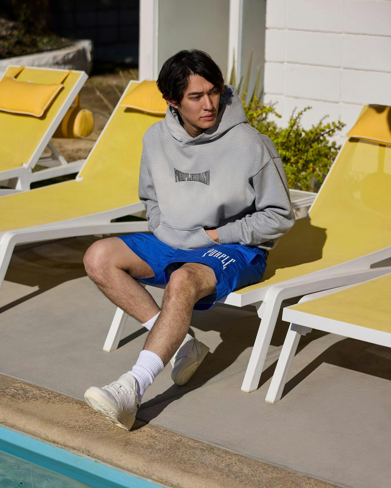 a man sitting on a chair next to a pool with a hoodie on