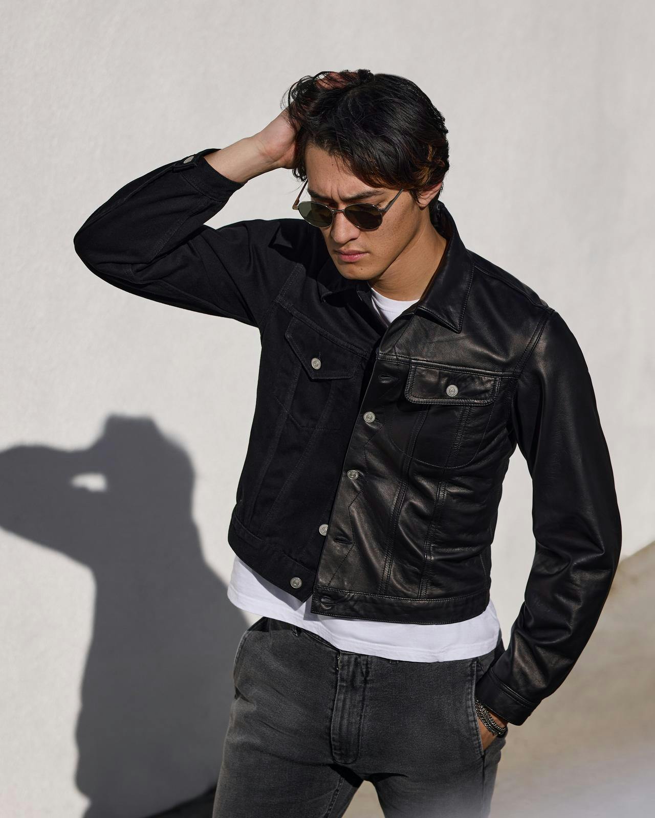 a man in a black leather jacket and sunglasses leaning on a wall