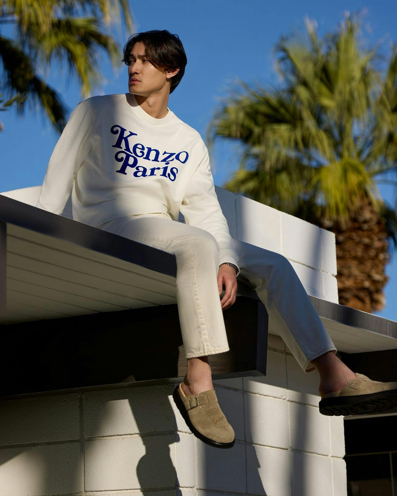a man sitting on a roof with a kenzo sweatshirt and jeans