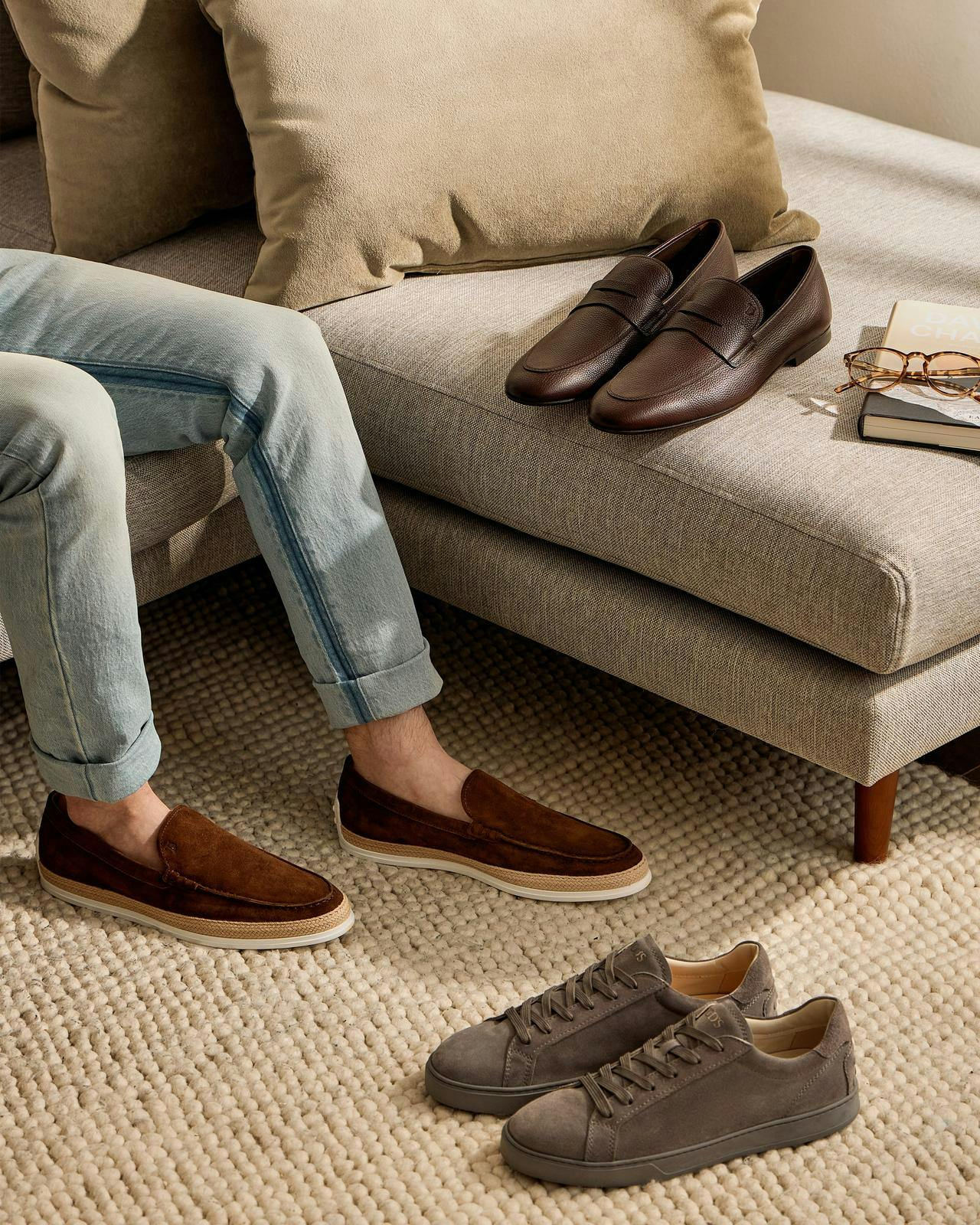 un homme assis sur un canapé avec quelques paires de chaussures autour