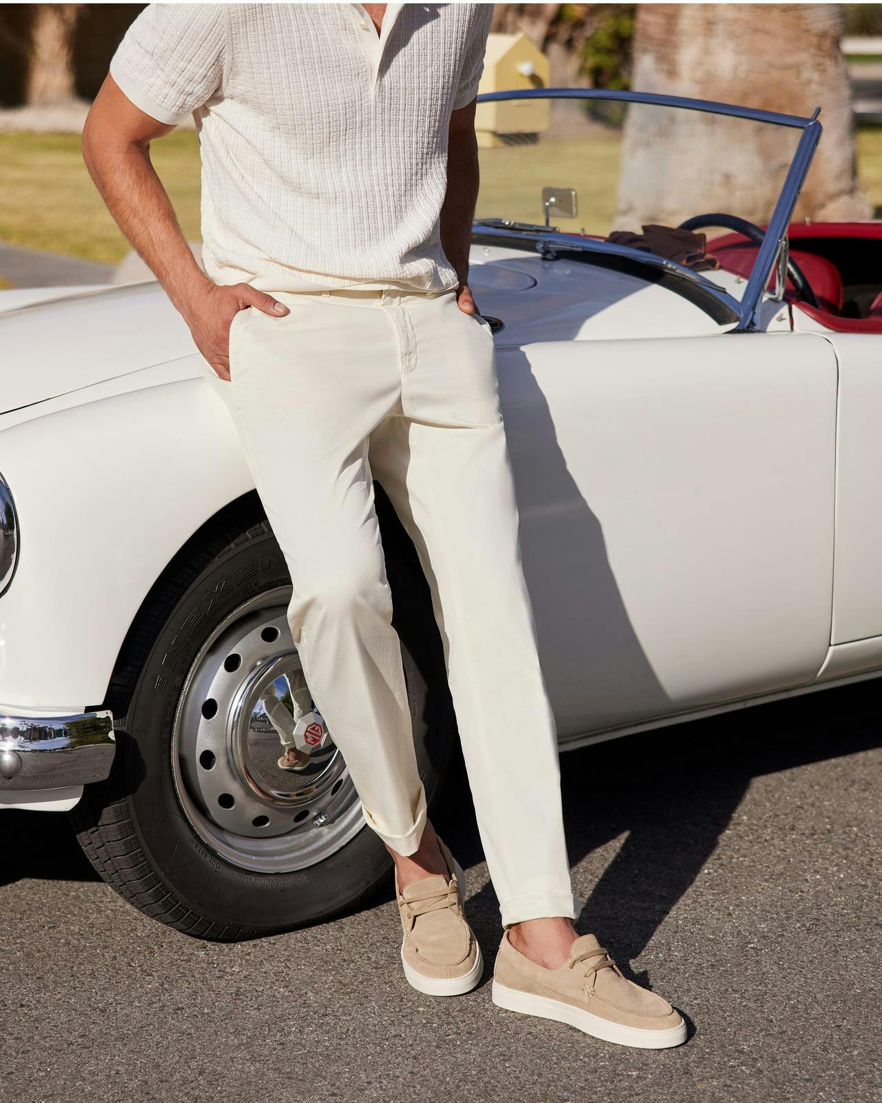 un homme appuyé contre une voiture blanche portant un pantalon blanc et un polo