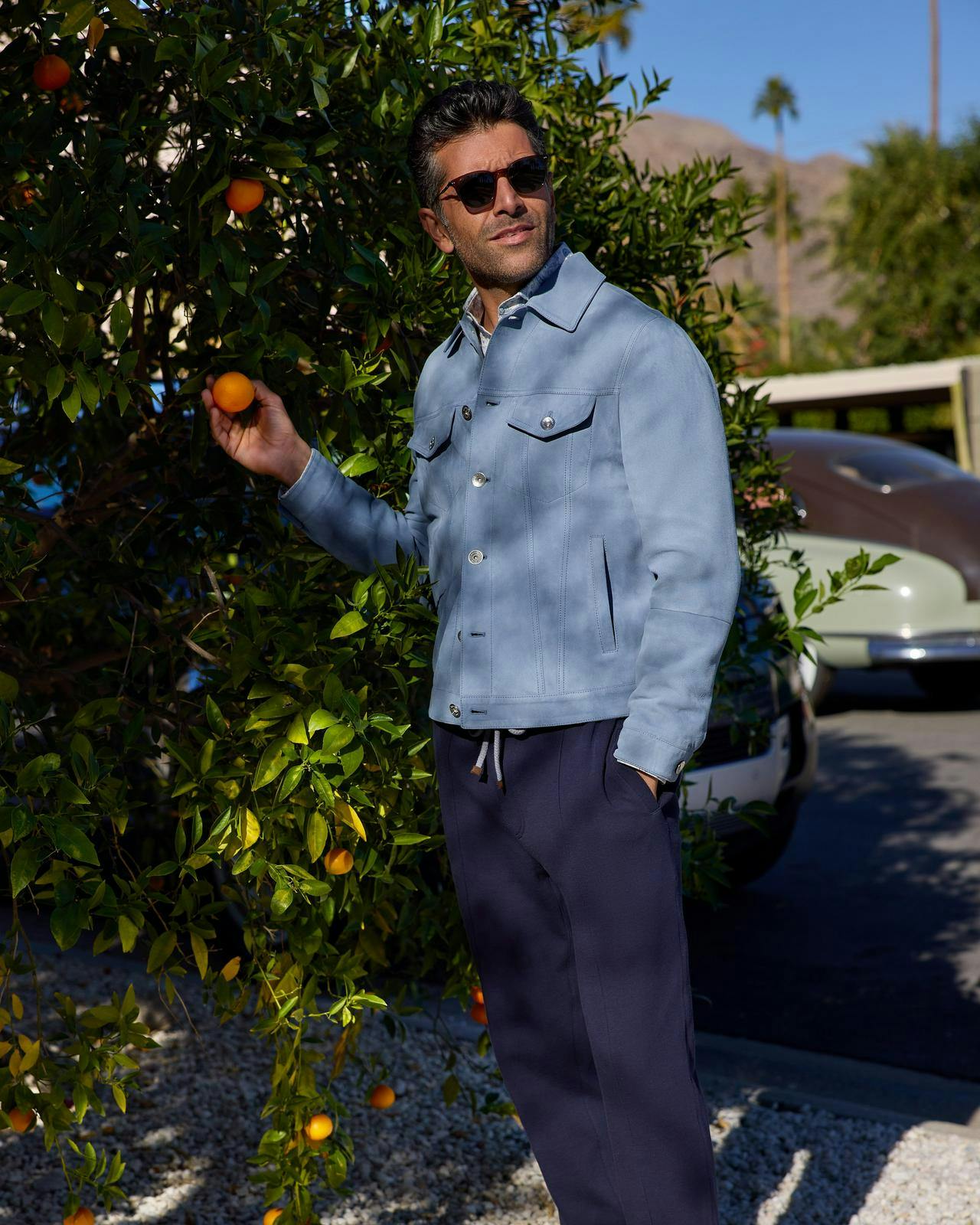 un homme vêtu d'une veste et d'un pantalon bleu clair tenant une orange