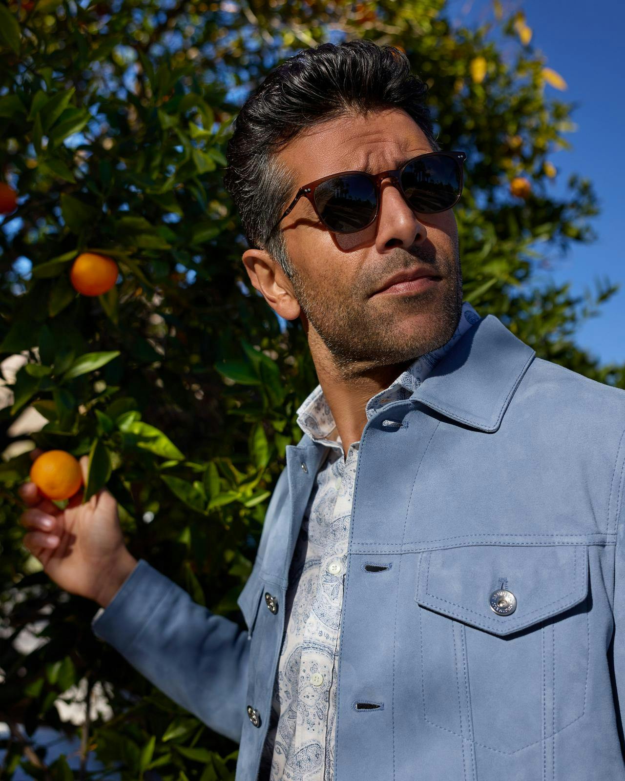 close up of a man wearing a light blue jacket holding an orange