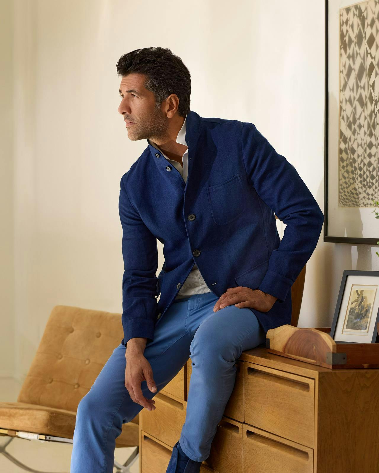 a man in a blue jacket and pants sitting on a dresser