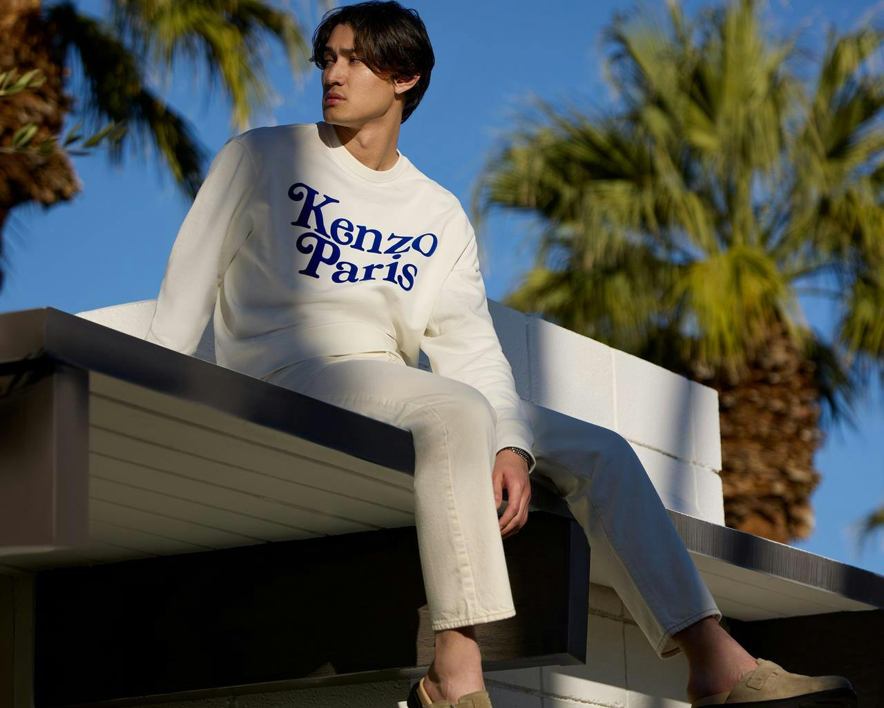 un homme assis au sommet d'un immeuble avec un sweat-shirt Kenzo blanc