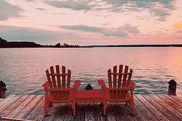 deux chaises de chalet classiques sur un quai en bois face au lac au coucher du soleil