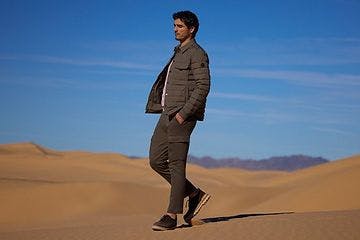 A man walking on a desert sand dune in a jacket